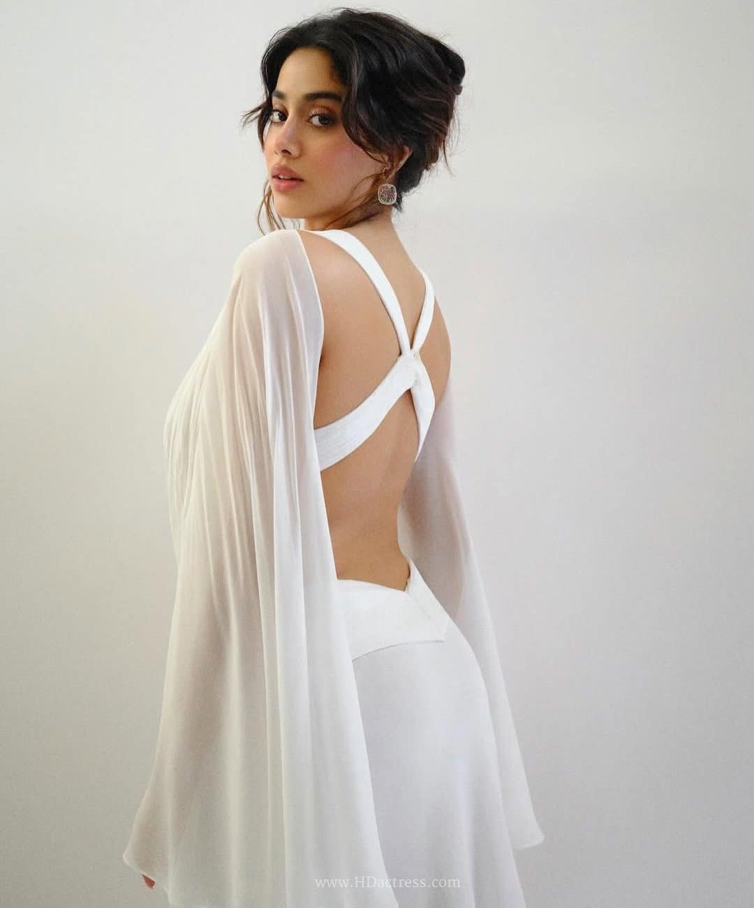 Janhvi Kapoor posing from behind to showcase a long flowing black maxi dress with a plunging open back and distinct wide supportive straps.