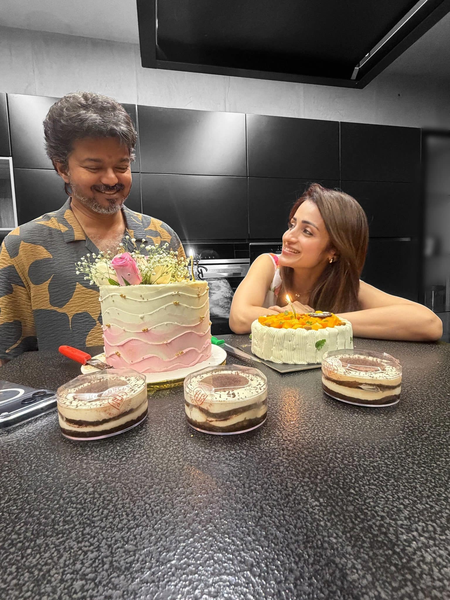Actress Trisha looking affectionately at Tamil Nadu CM Vijay as he smiles in front of multiple birthday cakes during a private midnight celebration.