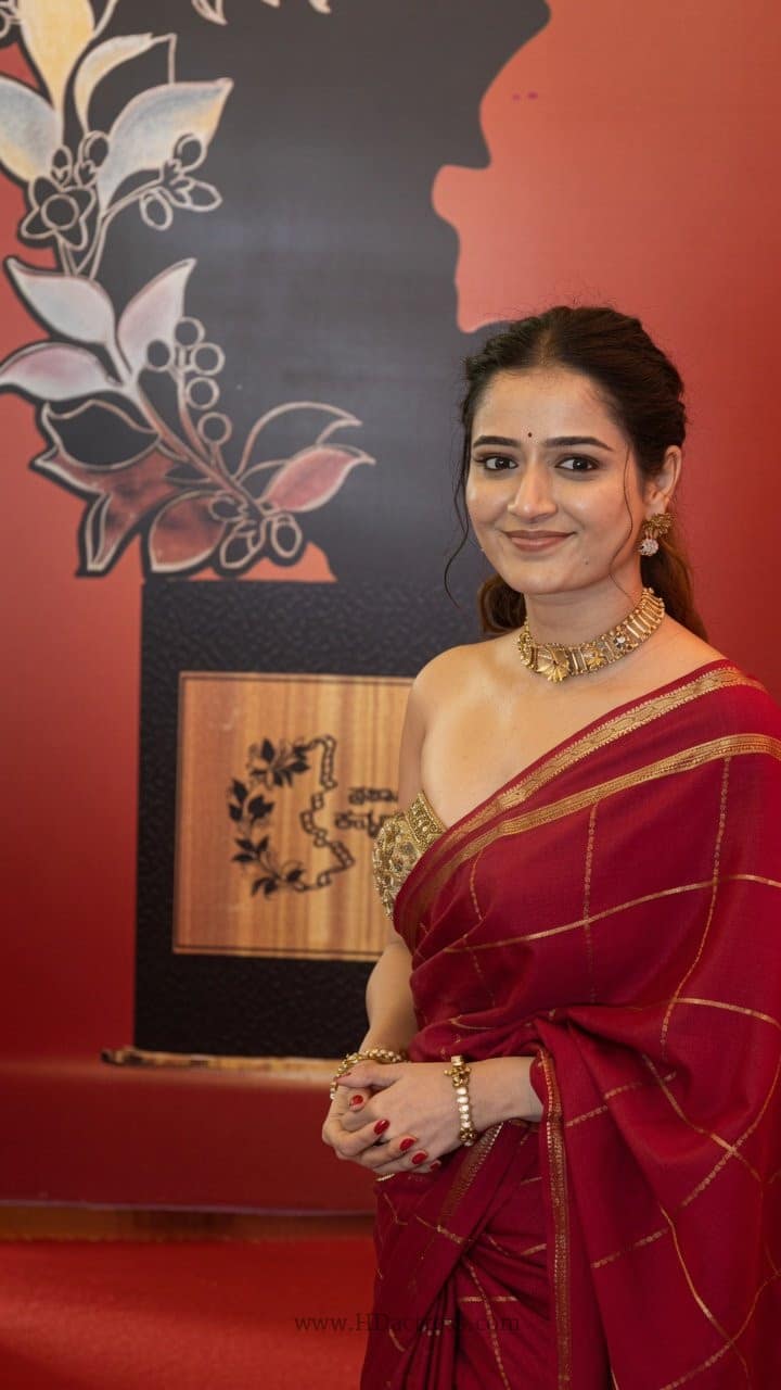 Ashika Ranganath looking glamorous in a modern red saree styling with minimal jewelry and a sleek sleeveless blouse.